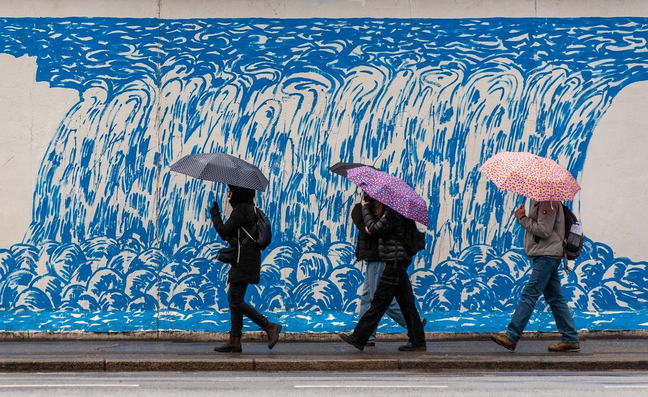 Quatre personnes marchent sous la pluie le long d'un trottoir à Porto au Portugal. Ils sont abrités par des parapluies colorés, et longent un mur bleu et blanc.