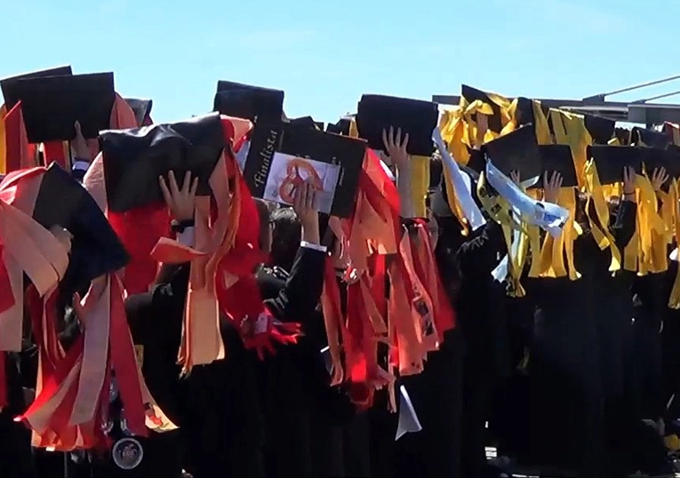 Photographie d'un groupe d'étudiants portugais brandissant leur chapeau orné de rubans aux couleurs de leur filière universitaire.